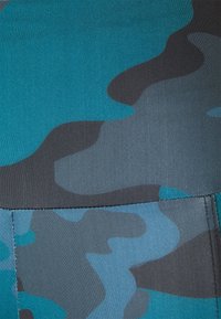 Tkanina s kamuflážním vzorem v odstínech modrozelené, šedé a černé. Hladký povrch s přiléhavým střihem a viditelným švem na spodní části.