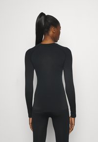 Fitted black long-sleeve top with textured pattern, round neckline, and raglan sleeves; paired with matching bottoms.