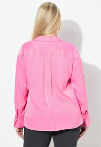 Langærmet bluse i lyserød satin med klassisk krave, lægdetalje bagpå og knapmanchetter. Stoffet har en glat, blank finish.