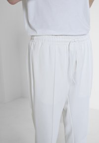 Witte sweatpants met een gestructureerde weving, voorzien van een elastische tailleband en een trekkoord. De zijnaad geeft de ontspannen pasvorm van de broek aan.