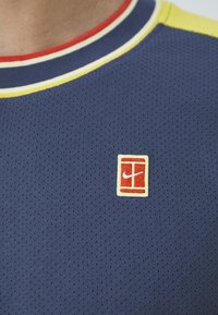 Námořnická modrá perforovaná tkanina tričko s límcem v červeno-bílé proužkované barvě. Má kulaté logo v červené a bílé barvě s Nike swoosh.