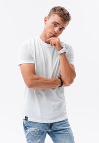 Vit bomull t-shirt med rund hals och korta ärmar, kombinerad med slitna blå jeans. Anmärkningsvärda accessoarer inkluderar en vit klocka och ett armband.