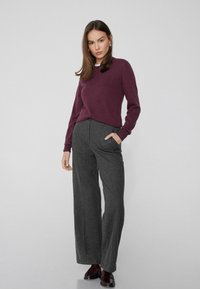 Pull en laine bordeaux avec encolure ronde, associé à un pantalon large gris taille haute. Le modèle porte des chaussures bordeaux et a les mains dans les poches.