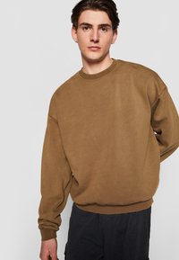 Brun sweatshirts med rund halsudskæring, dropped shoulders og ribbede manchetter. Stof ser blødt ud med en glat tekstur.