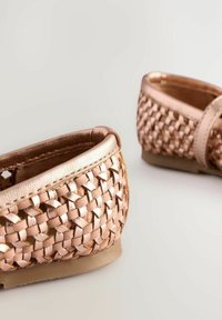 Vävda sandaler i roséguld med en slät läderkant, med en rundad form och en platt gummisula, som visar en texturerad design.