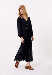 Navy doorschijnende blouse met poffende mouwen en knopen, gecombineerd met een bijpassende rok met een strikdetail. Bruine block-heeled sandalen.