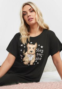 T-shirt nera a maniche corte con una grafica di un cane dei cartoni e il testo "Stay paw-sitive," circondato da motivi di stelle.