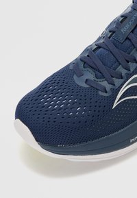 Zapatilla de correr de malla color navy con perforaciones para transpirabilidad, superficie texturizada, ojales reforzados y suela de goma blanca.