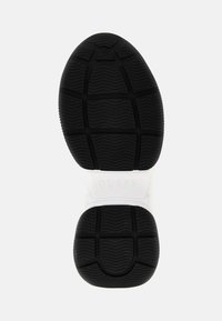 Semelle de chaussure en caoutchouc noir avec un motif de bande de roulement texturé, semelle intermédiaire blanche avec logo "GUESS" embossé, design épuré et forme arrondie.