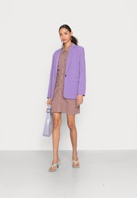 Blazer lavanda, vestido mauve texturizado com botões, sandálias de salto alto verde claro e uma mala lavanda brilhante. Materiais suaves, design contemporâneo.