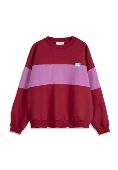Sweat-shirt rouge avec une large bande horizontale lavande sur la poitrine et les manches, arborant un petit patch logo rectangulaire bleu sur la poitrine gauche.