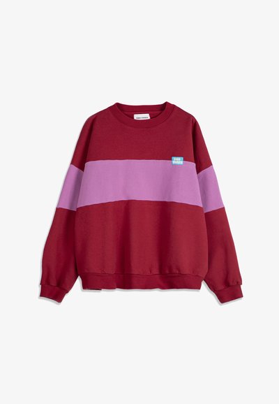 Sweat-shirt rouge avec une large bande horizontale lavande sur la poitrine et les manches, arborant un petit patch logo rectangulaire bleu sur la poitrine gauche.