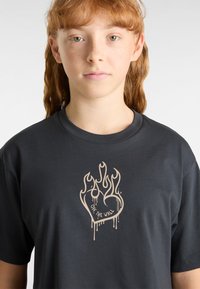 Black cotton t-shirt featuring a central beige flaming heart graphic with "OFF THE WALL" text and drips, round neck design, short sleeves.