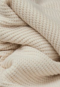 Beżowy materiał o fakturze z prążkowanym wzorem, miękki i puszysty, ukazujący warstwowe zgięcia, które tworzą głębię i wizualne zainteresowanie.