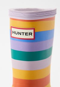 Viacfarebná gumová čižma s horizontálnymi pruhmi v žltej, oranžovej, zelenej, modrej, fialovej a ružovej farbe, s bielou nálepkou "HUNTER".