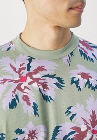 Grünes Baumwoll-T-Shirt mit einem großen, bunten Blumenmuster in den Farben Pink, Lila, Burgunder und Grün sowie einem gerippten Rundhalsausschnitt.