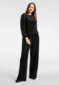 Czarny zestaw do wypoczynku z cekinami, składający się z bluzki z długim rękawem i okrągłym dekoltem oraz spodni o szerokich nogawkach. Miękka tekstura z błyszczącym wykończeniem.