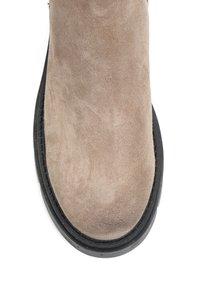 Jasnobeżowy zamszowy but o gładkiej fakturze i zaokrąglonym nosku, z czarną gumową podeszwą i subtelnym przeszyciem wzdłuż krawędzi.