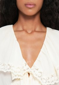 Witte blouse met een diepe V-hals, voorzien van een kanten rand langs de kraag en geplooide stofdetails. Glad, lichtgewicht materiaal.