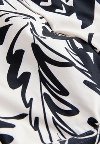 Motif de feuille abstraite noire sur tissu blanc avec des plis doux et des détails de couture visibles.