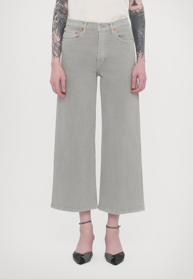 Jean large gris clair à taille haute, avec un design à cinq poches et des accents de couture orange. Associé à des ballerines noires à bout pointu.