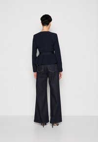 Námořnický peplum top s přiléhavým pasem, zkombinovaný s širokými tmavými džíny. Outfit má dlouhé rukávy a hladkou texturu látky.