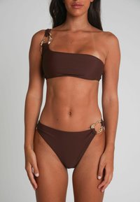 Brun bikini-set med en axelbandsöverdel och matchande underdelar. Har guldfärgade detaljer, slät textur och en enkel design.