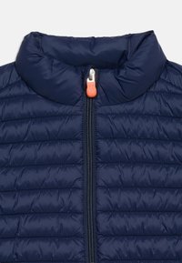 Καπιτονέ μπουφάν σε ναυτικό μπλε με ψηλό γιακά και μπροστινό φερμουάρ με πορτοκαλί γαντζάκι.