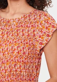 Kukallinen mekko pyöreällä pääntiellä, jossa on taitettu malli persikan, vaaleanpunaisen, oranssin ja punaisen väreissä, valmistettu kevyestä kankaasta. Lyhyet hihat.