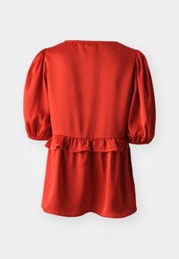 Κόκκινο μπλουζάκι με μακριά μανίκια και φουσκωτά μανίκια, τετράγωνο ντεκολτέ και βολάν στη μέση, φαίνεται από πίσω σε λευκό φόντο.