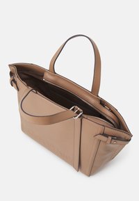 Sac fourre-tout en cuir tan avec deux poignées supérieures, fermeture éclair ouverte et logo en relief. L'intérieur comprend un compartiment doublé et une poche zippée.