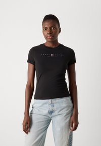 Černé přiléhavé tričko s krátkým rukávem a kulatým výstřihem, s bílým nápisem „TOMMY JEANS NEW YORK CITY“ na přední straně.