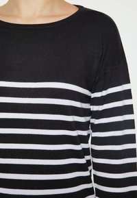Maglione a righe bianche e nere con collo rotondo, texture lavorata a maglia e maniche lunghe. Le righe sono equidistanti e orizzontali.