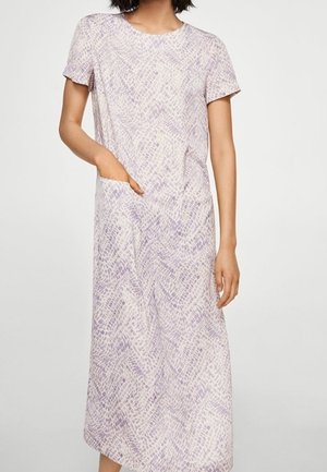 Kobieta w fioletowej, krótkorękawowej sukience midi z wzorem, z okrągłym dekoltem i przednią kieszenią, stojąca na jednolitym tle.