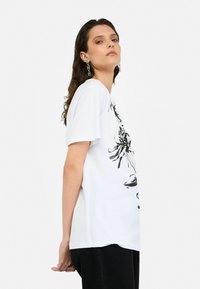Tricou alb din bumbac, cu imprimeu grafic negru îndrăzneț, mâneci scurte, croială lejeră și guler rotund. Accentuat cu detalii de design texturat.