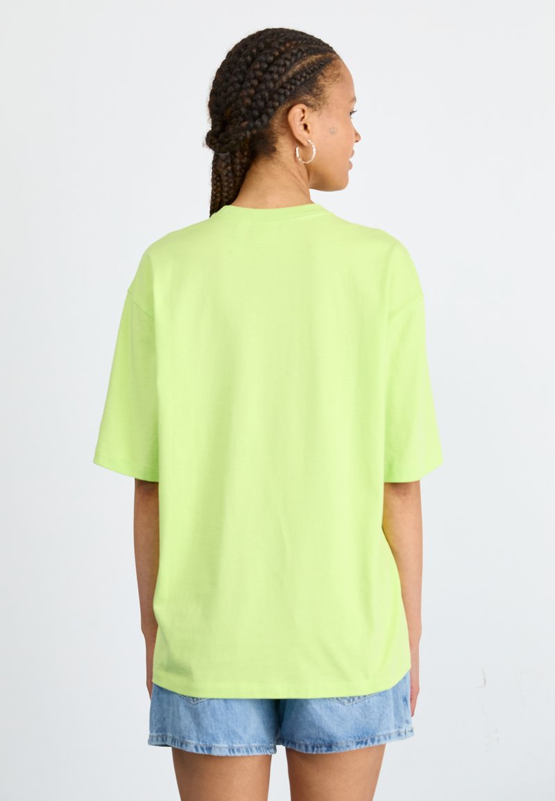 Jasnozielona, luźna koszulka z bawełny, z krótkimi rękawami, okrągłym dekoltem i swobodnym krojem, noszona z dżinsowymi szortami.