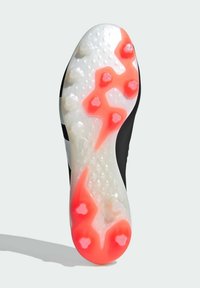 Svart fotbollssko med en genomskinlig vit sula, prydd med röda accenter och flera formade dobbar för bättre grepp. Texturerad design genom hela skon.