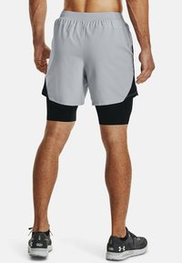 Grå löparshorts med elastisk midja, foder och svarta accenter; kombinerat med svarta kompressionsshorts och löparskor.