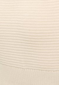 Světlé béžové pletené látky s horizontálními žebrováními a vertikálními texturálními variacemi. Měkký, elastický materiál, zakončený silnějším žebrovaným lemem.