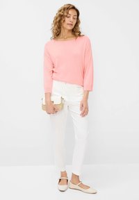Lichtroze top met driekwartmouwen, witte slim-fit broek, beige balletschoenen en een kleine glinsterende gouden clutch. Eenvoudig en modern ontwerp.