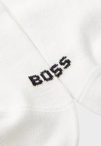 Hvite sokker laget av en bomullsblanding med ribbet tekstur, med "BOSS"-logo i svart strikk på siden.