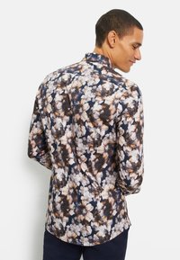 Overhemd met knopen en een bloemenpatroon in tinten beige, wit en bruin op een marineblauwe achtergrond. Gemaakt van lichtgewicht stof met een kraag.