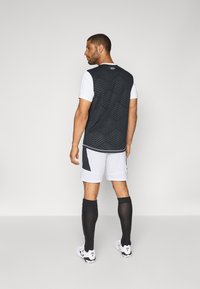 Schwarzes und weißes Sportoutfit mit einem strukturierten, rautenförmigen ärmellosen Oberteil, weißen Shorts und schwarzen knielangen Socken.