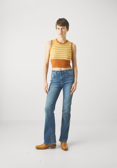 Top scurt tricotat în portocaliu și crem, cu o margine cu textură ribbed, asortat cu blugi evazați de culoare albastră deschisă și pantofi din piele bej. Design și textură simplă.