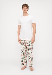 Fehér, rövid ujjú póló, amelyet mintás pizsama nadrággal párosítottak, téli jelenetekkel, fákkal és fakó házakkal zöld, piros és rózsaszín árnyalatokban.