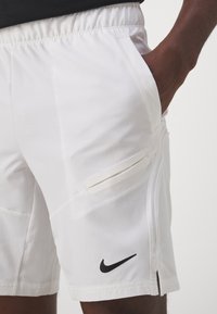 Shorts atléticos blancos con una cinturilla elástica, bolsillos laterales y un logo negro de Nike en la cadera. Tejido suave con un ligero brillo.