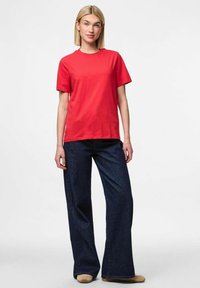 Rød bomulds T-shirt med korte ærmer, parret med mørkeblå vide jeans. T-shirten har en rund halsudskæring og en afslappet pasform.