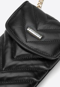 Bolso de cuero negro con diseño acolchado, con placa de logo en hardware plateado. Correa de cadena adjunta. Textura suave con costuras definidas.