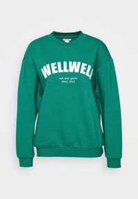 Grön sweatshirt med rundad halsringning, med fet vit text "WELLWELL" och "inte intresserad av sport sedan 2002" tryckt på framsidan.