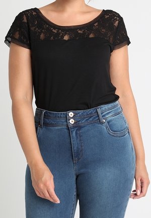Czarny top z koronkowymi rękawkami typu cap, okrągłym dekoltem i miękkim materiałem. Połączony z wysokim stanem niebieskich dżinsów z dwoma guzikami.